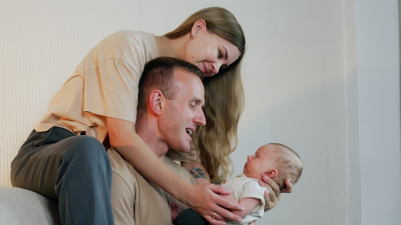 Lovely newborn baby in dad's arms looks at his parents. Smiling couple making faces to a kid.
