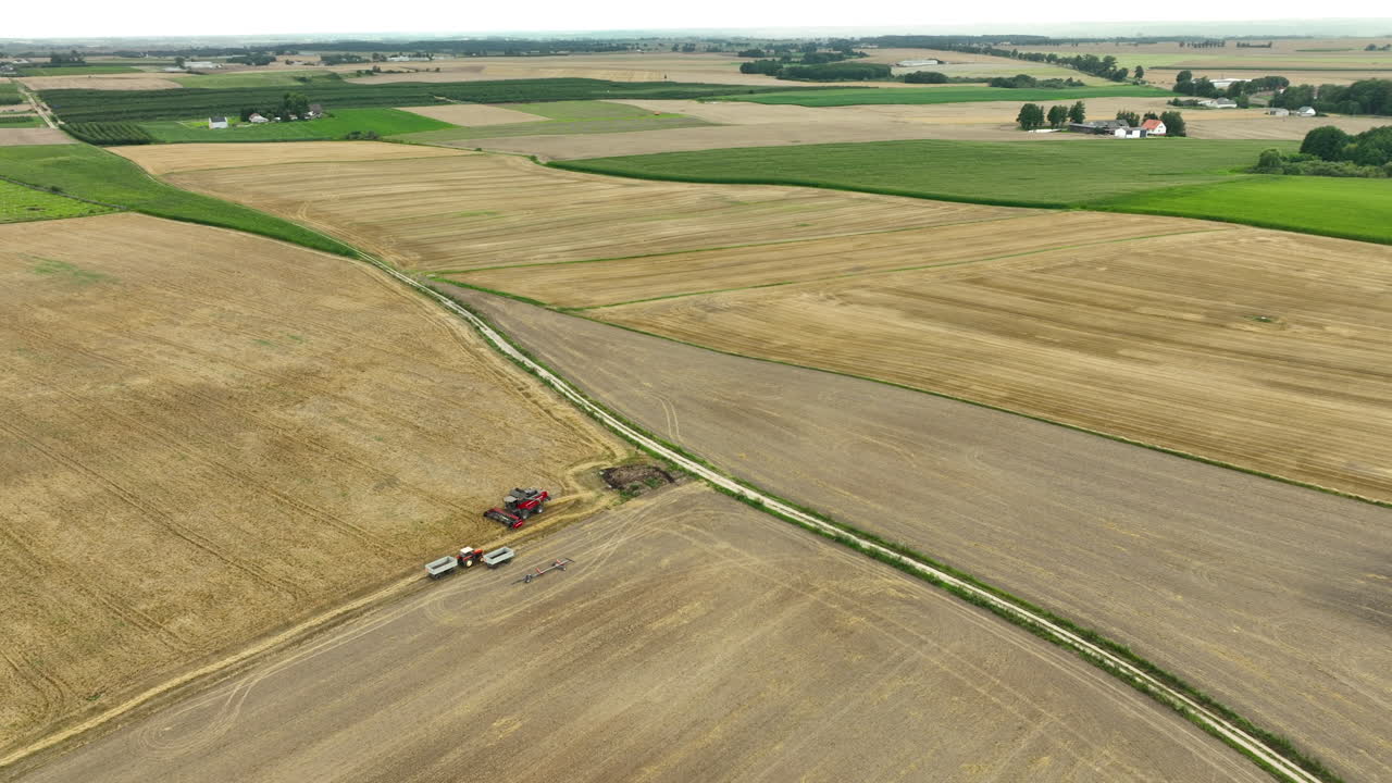 Aerial view of a combine harvester working in a wheat field near a dirt road. The vast agricultural landscape showcases the scale and organization of modern farming