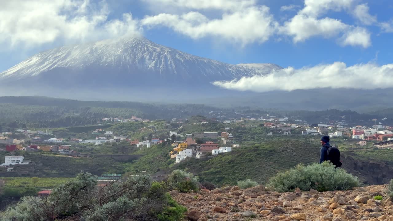 Escursionista solitario con uno zaino che si gode la vista panoramica del vulcano Teide innevato a Tenerife, Isole Canarie, in una giornata luminosa.