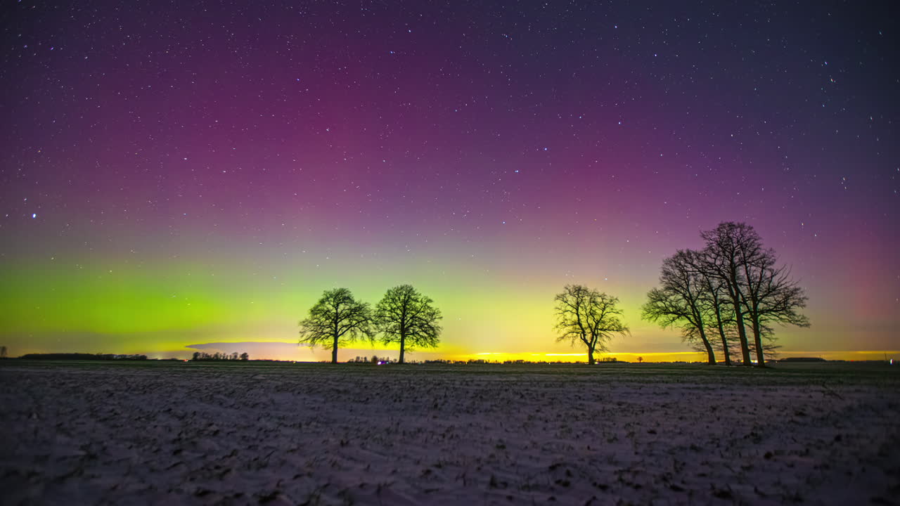 Awesome timelapse of a colorful night sky with bright aurora borealis and stars over trees and a field in Sri Lanka