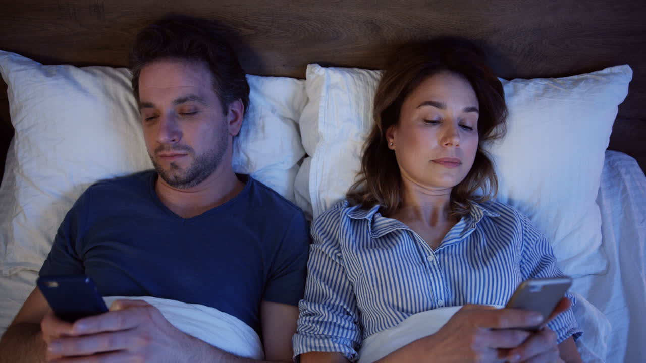 Top view of caucasian couple lying on the bed and using smartphones at night