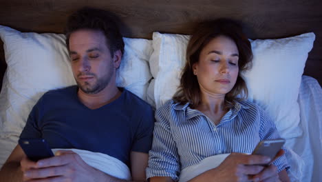 top view of caucasian couple lying on the bed and using smartphones at night