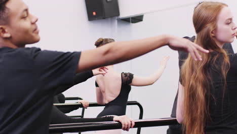 male and female students at performing arts school rehearse ballet with teacher in studio with barre