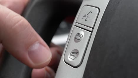 an extreme close up of the talk and handsfree buttons on a cars steering wheel and a white caucasian hand pushing the buttons