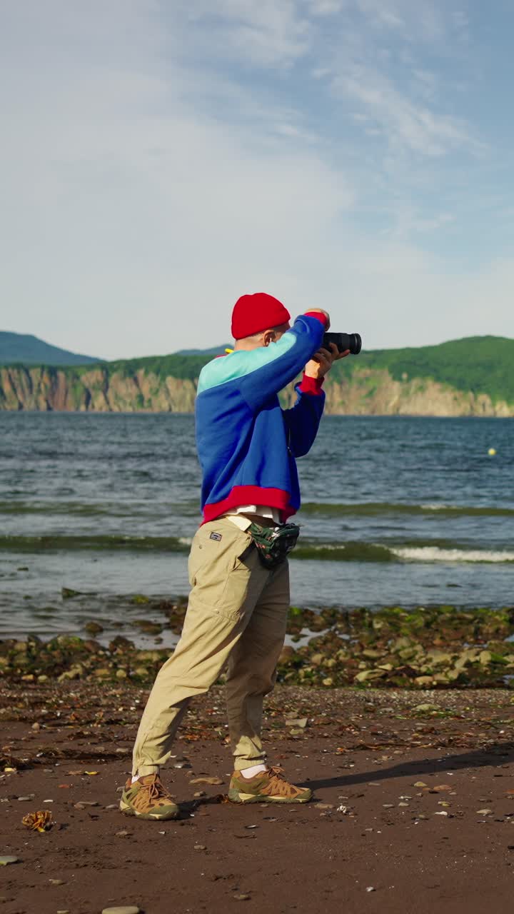 Man Taking Photos on a Scenic Beach with Ocean and Mountains