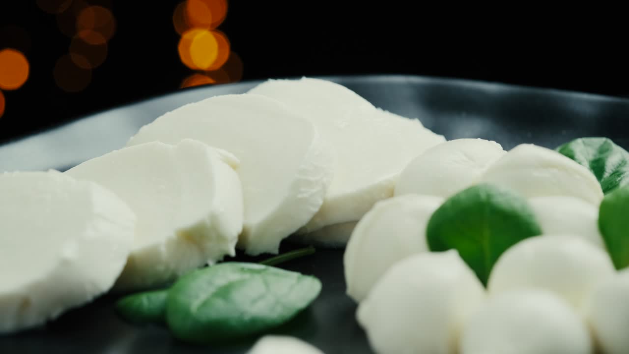 pequeñas bolas de queso mozzarella blancas, hojas de espinaca en un plato negro.