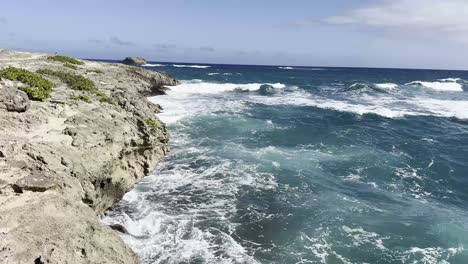 Waves-crash-against-the-rugged-coastal-cliffs-of-Oahu,-creating-a-dynamic-and-vibrant-seascape-with-clear,-deep-blue-waters