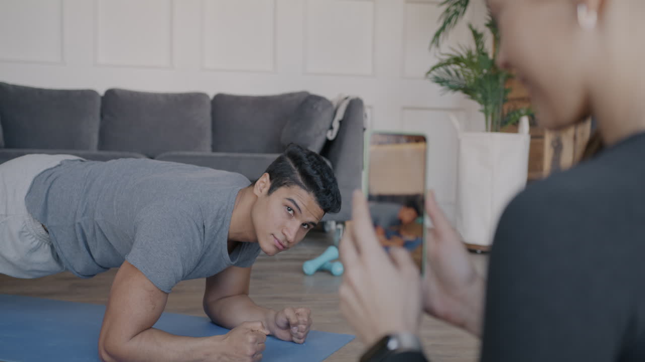 Man doing plank exercise, being filmed by a woman