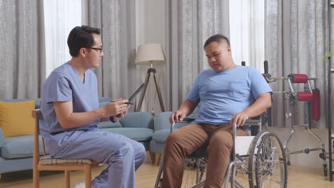 side view of asian male nurse and patient in wheelchair talking about medical test results on a tablet after physical therapy at home