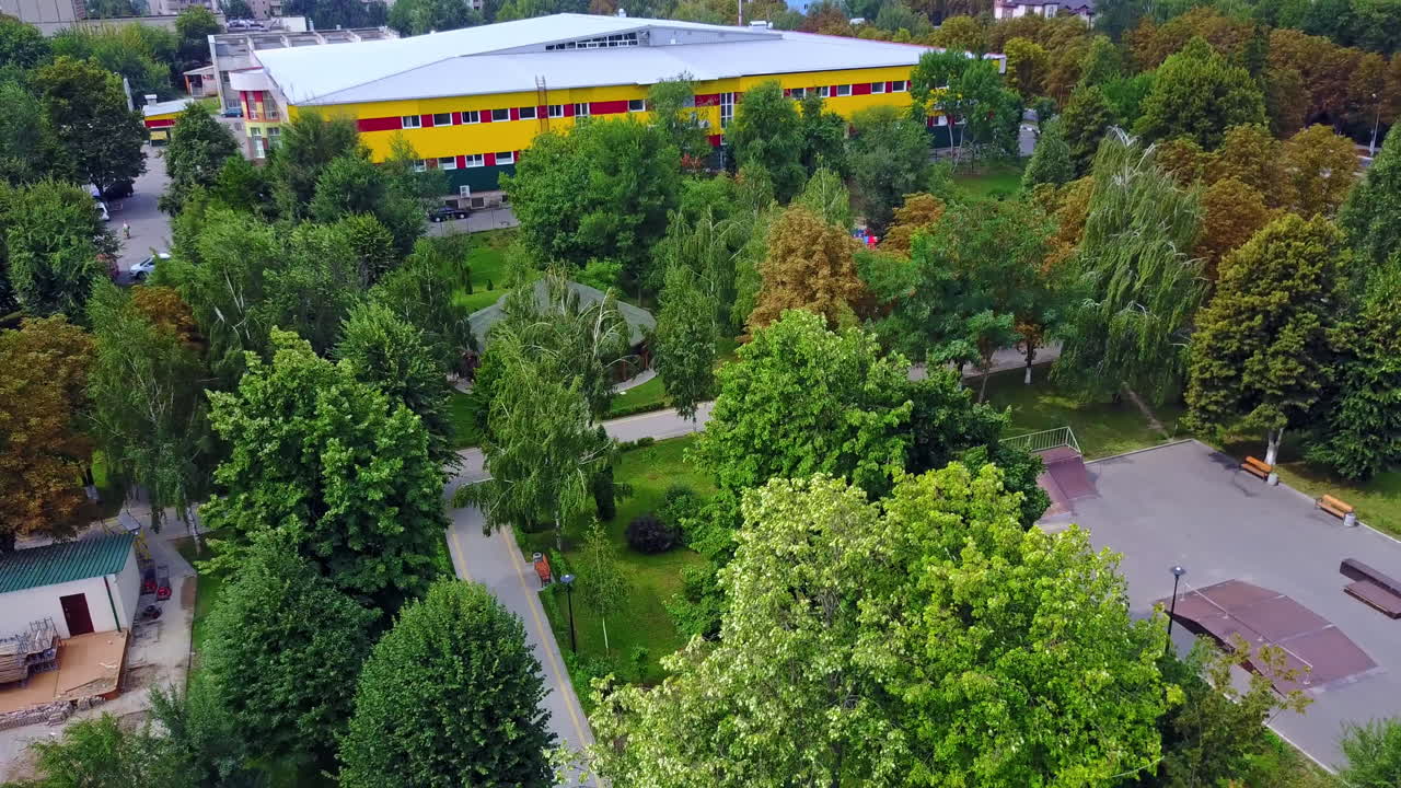 Strong wind waving the trees in the city park. Two-storied yellow building at backdrop. Top view.