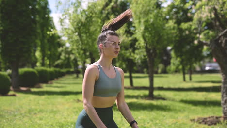 schöne brünette frau, die im park sprungkniebeugen macht, ihre smartwatch beobachtet und eine pause macht