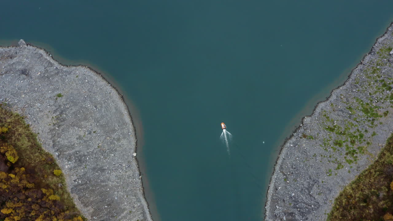 Narrow river winding between forested hills with shallow green water and curved flow, aerial top shot as boat exits estuary