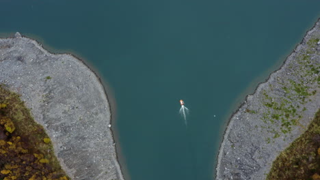narrow river winding between forested hills with shallow green water and curved flow, aerial top shot as boat exits estuary