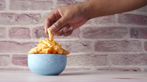 hand picking a chip from a bowl of crispy snacks