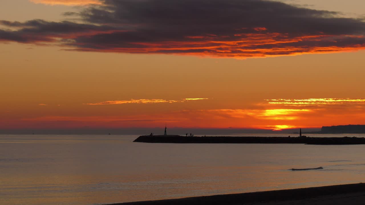 Sol saliendo sobre un océano en calma hacia cielos nublados anaranjados, paisaje marino