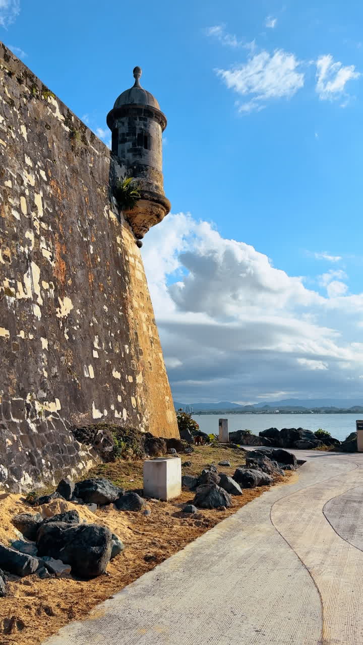 Cammina lungo l'alta muraglia con una torre dell'antica fortezza. Paesaggio acquatico sotto il cielo nuvoloso sullo sfondo. Video verticale