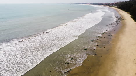 Aerial-flight-along-sandy-beach-of-Vietnam-with-washed-up-dirt,-net-and-trash-on-shoreline