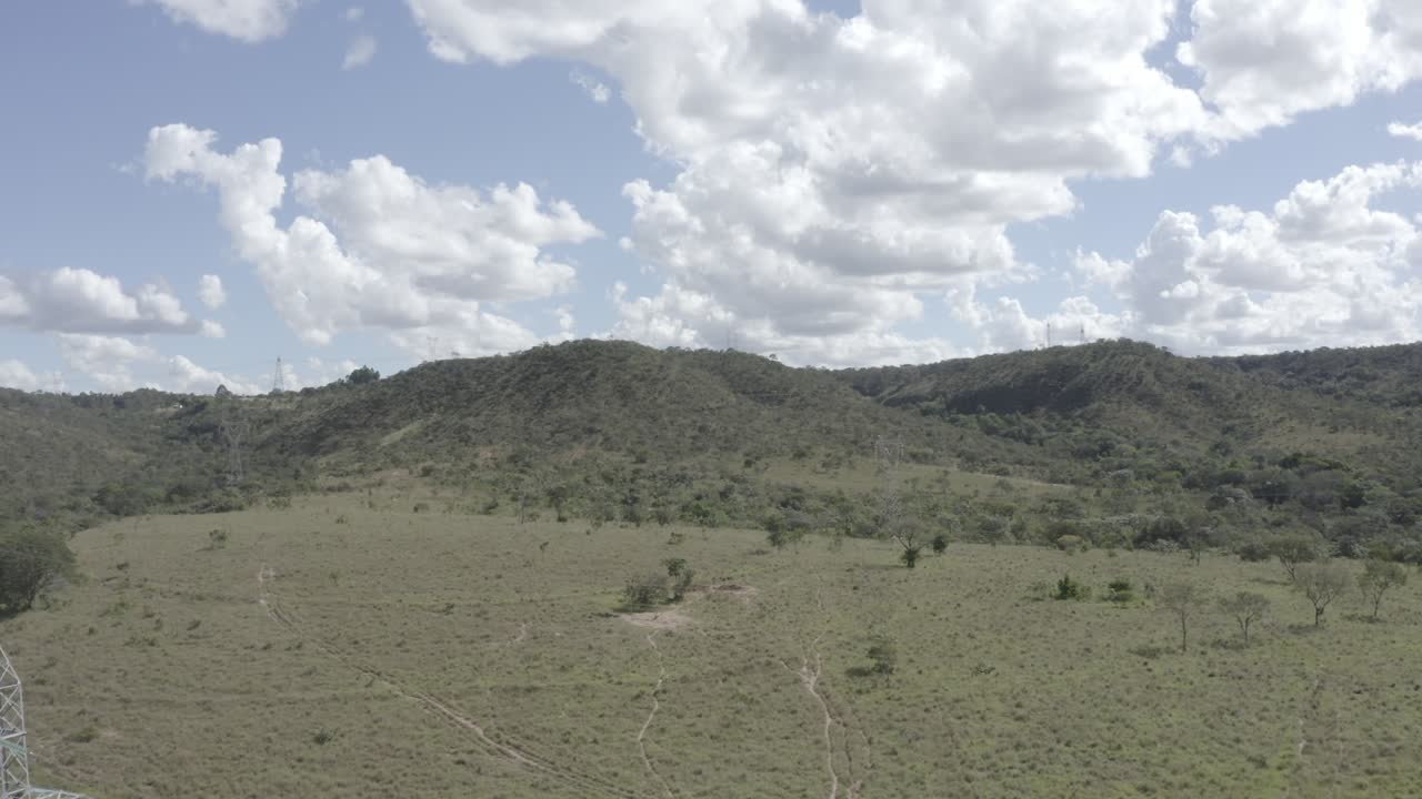 Cerrado reserve in Goiás with dry grassy terrain, sparse vegetation, and a transmission tower showing biome exposure and infrastructure contrast in Brazil’s central savanna, drone shot