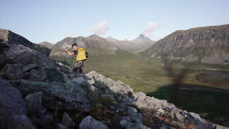 side view of hiker ascending hillside, early autumn morning, mountain background