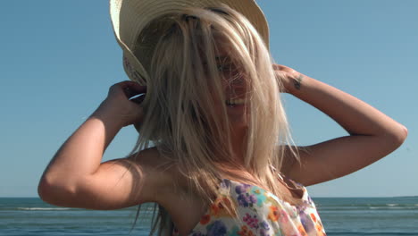 Attractive-blonde-turning-with-straw-hat-on-beach