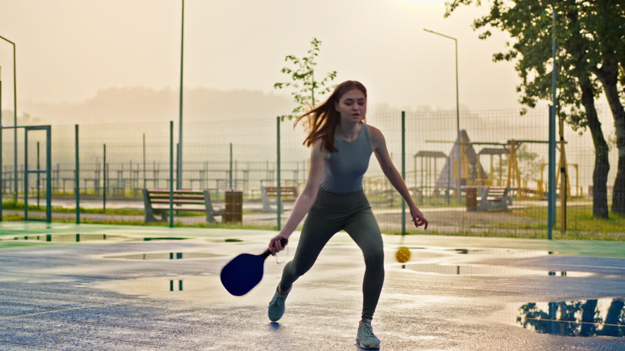 Woman playing pickleball on a blue and green court after rain
