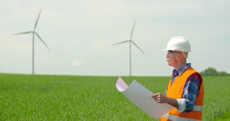 engineer analyzing plan while looking at windmills in farm