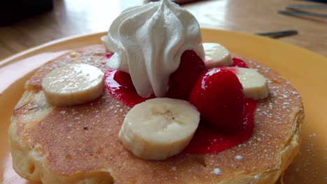close-up zoom out of pancakes topped with banana, strawberries and whipped cream.