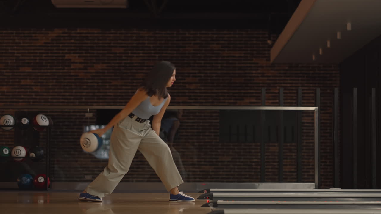 Alone Caucasian brunette woman throws a bowling ball and knocks out a shoot with one throw dances rejoices and jumps with happiness