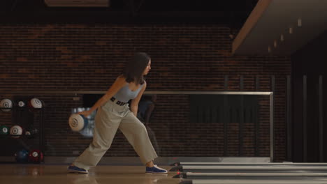 alone caucasian brunette woman throws a bowling ball and knocks out a shoot with one throw dances rejoices and jumps with happiness