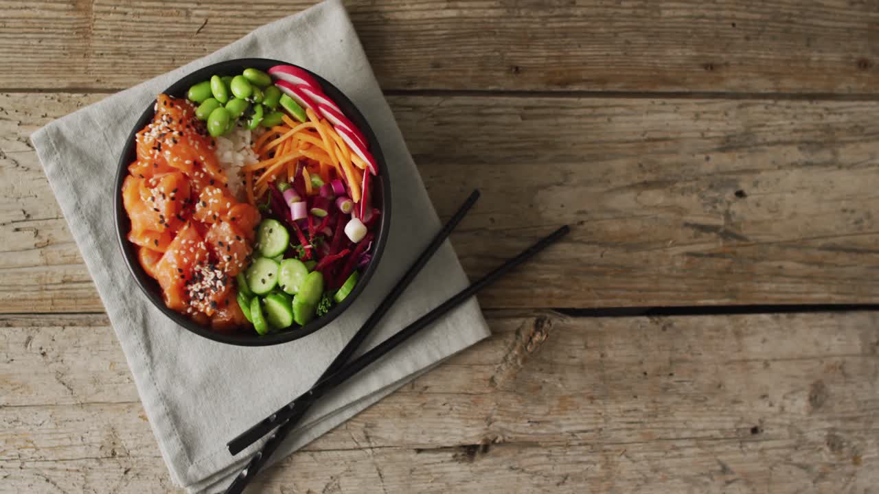 Composition of bowl of rice, salmon and vegetables with chopsticks on wooden background