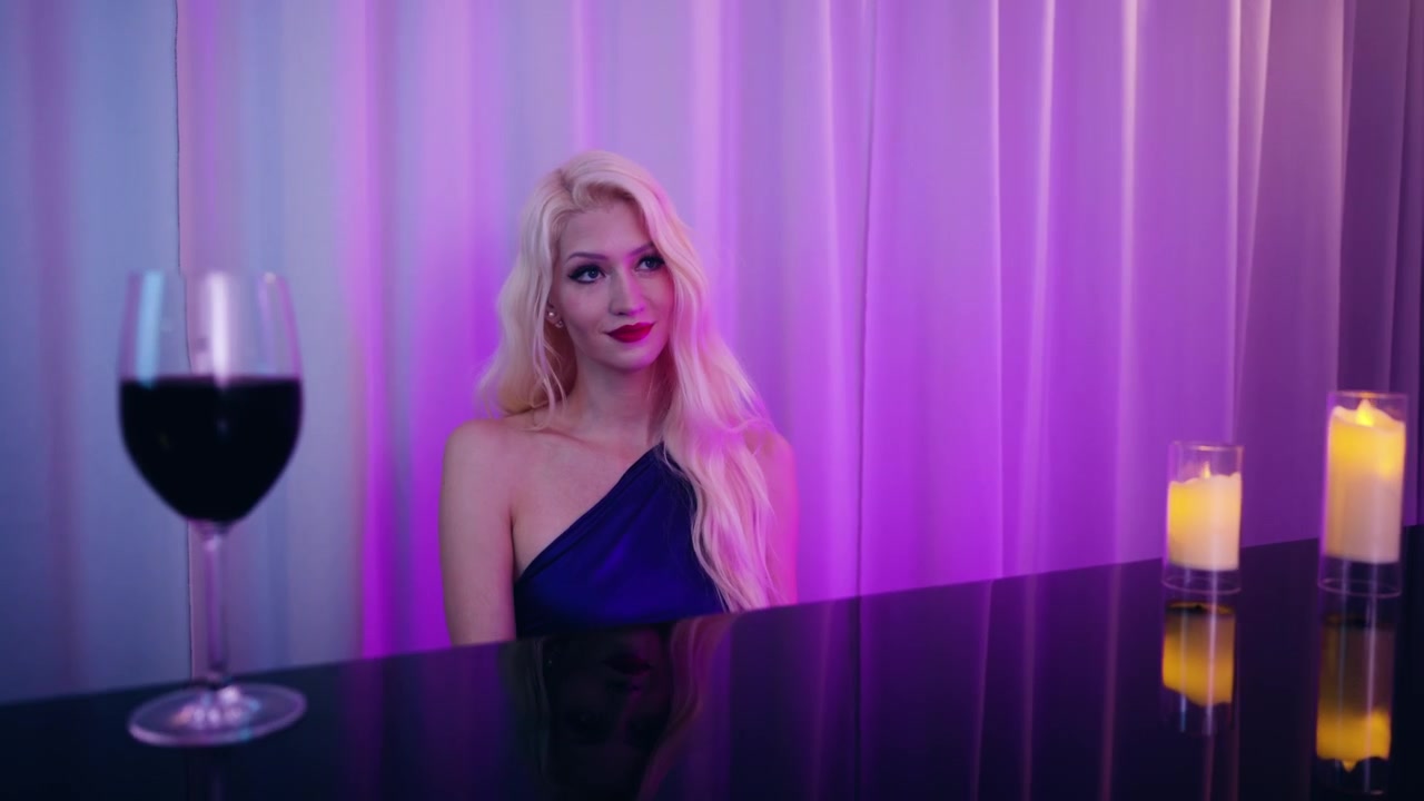 Elegante giovane pianista che si esibisce da solo sul palco con un pianoforte a coda in un lounge notturno illuminato da luci soffuse viola e blu.