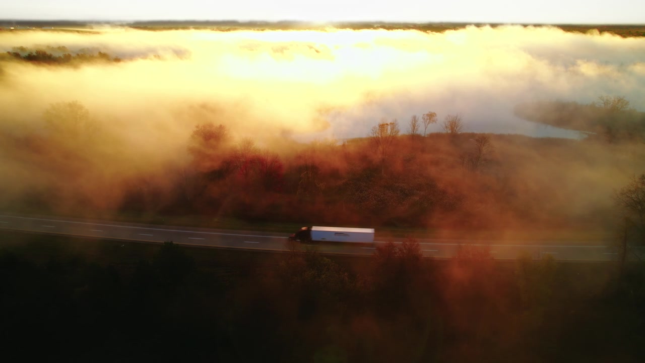 Tir che trasporta un rimorchio su un'autostrada nebbiosa all'alba, incorniciato dal fogliame autunnale e dalla luce dorata