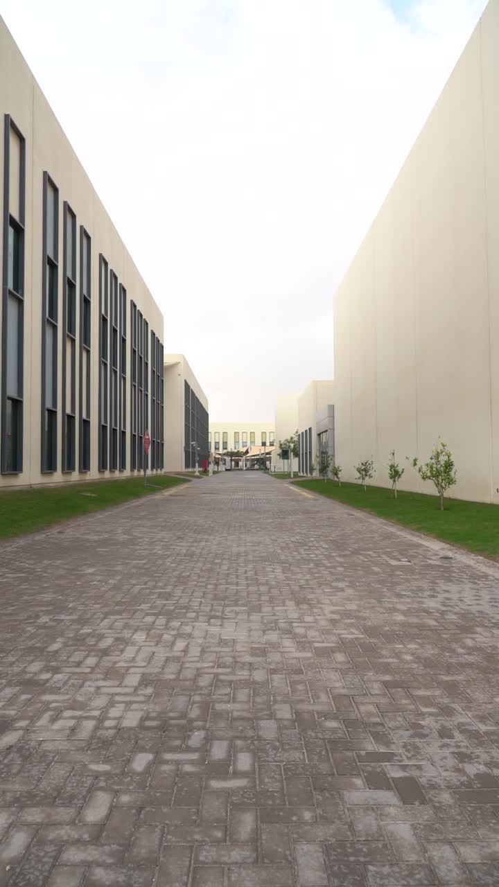Un sendero pavimentado sin gente serpenteando a través de un campus educativo o corporativo. Presenta un diseño contemporáneo, bordes de césped cuidados y una atmósfera tranquila y serena.