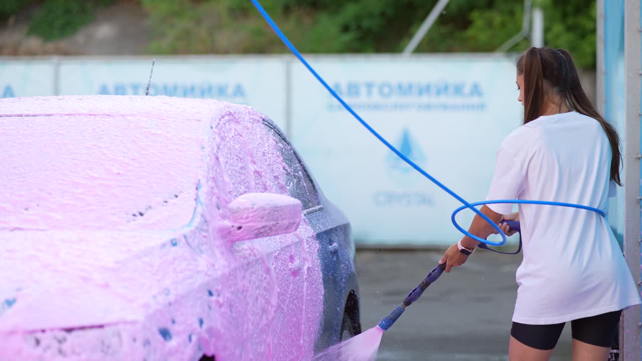 mujer lavando coches con espuma rosa en un lavado de coches de autoservicio