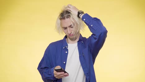 a young man in a blue shirt thoughtfully scrolling through his smartphone and not satisfied with what he sees