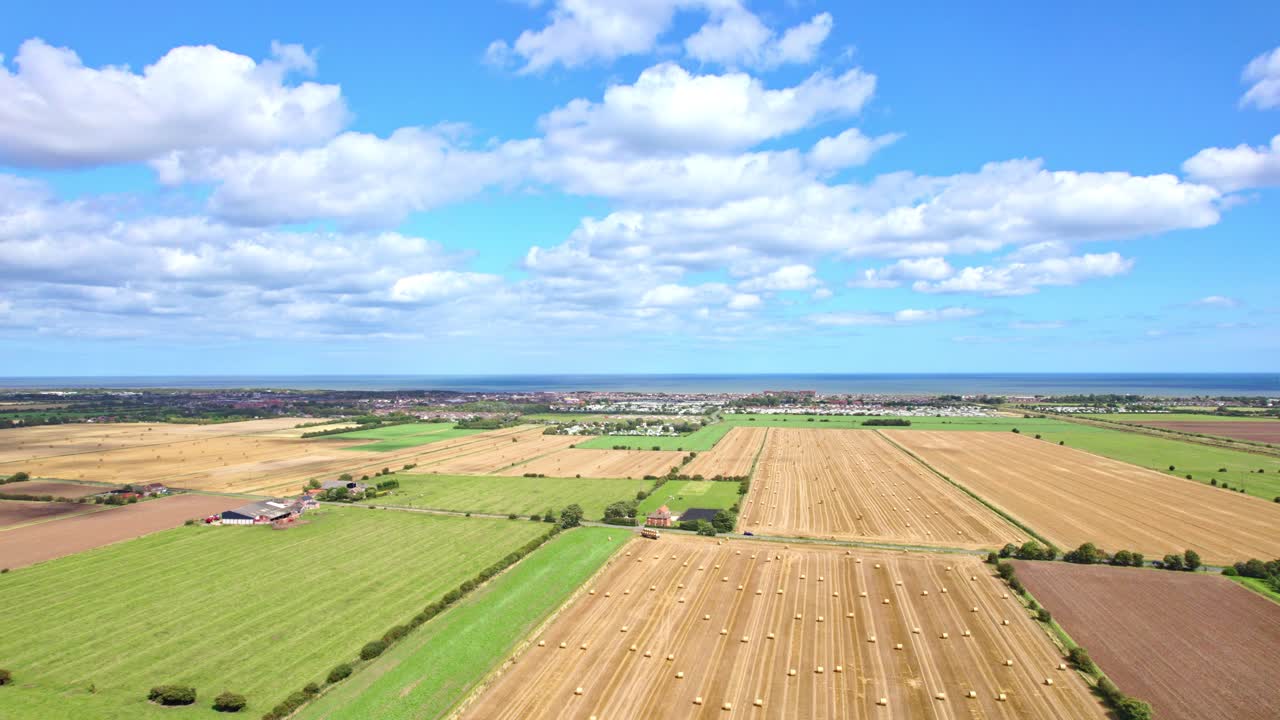 Aerial video footage paints a mesmerizing picture with wind turbines in a row, gently spinning amidst a Lincolnshire farmer's freshly harvested field, framed by golden hay bales