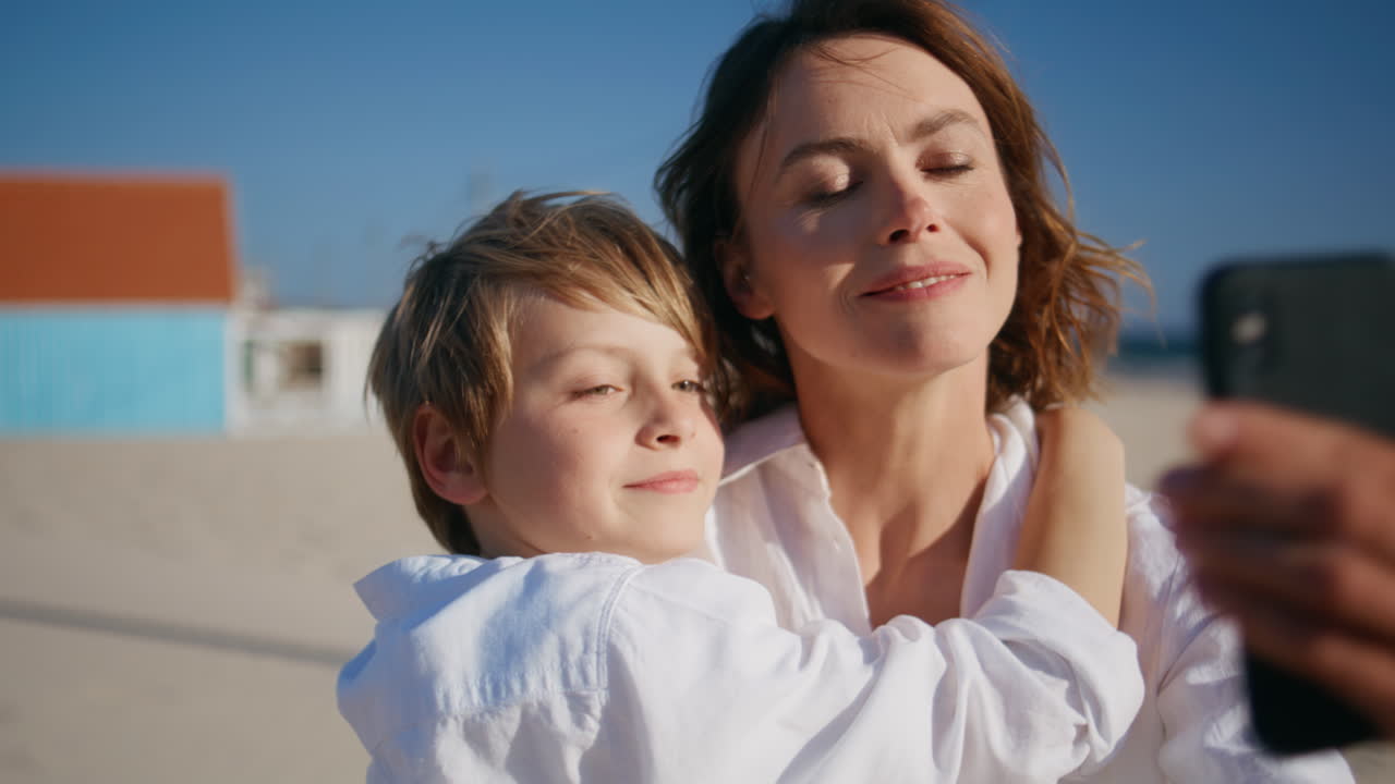 Nahaufnahme: Mutter und Kind streamen mit dem Handy und genießen den Sommerurlaub am Strand