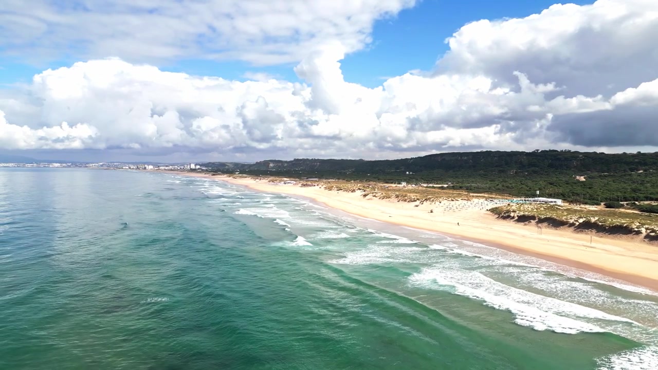 Luftfoto glider langs Praia da Morena kystlinje, viser bølger og sandstrand