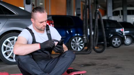 auto mechanic uses a smartphone he sits and rests from work car service auto mechanic uses a smartphone he sits and rests from work car service