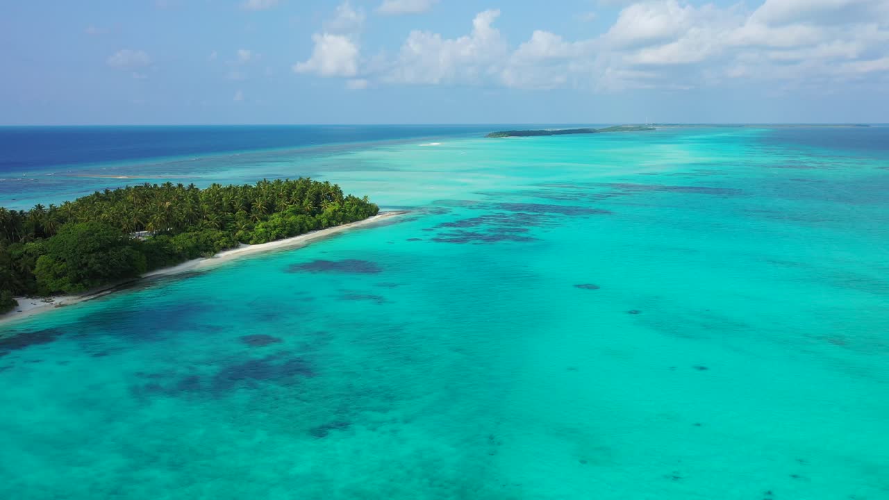 Paradise azure lagoon with calm clear water and coral reefs patterns around tropical island with lush vegetation and white sandy beach on a bright sky with clouds