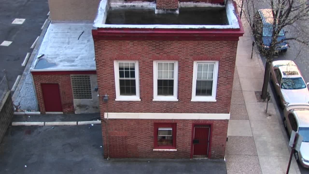 la cámara mira hacia abajo y luego hace zoom en un pequeño edificio antiguo de dos pisos y en las ventanas del segundo piso