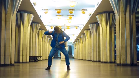 stylish guy with glasses fashionably dancing and waving his arms in the subway. young man listens to music with headphones and jumps at the station.