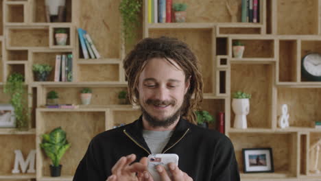 portrait of young attractive man with dreadlocks browsing social media using smarphone smiling cheerful