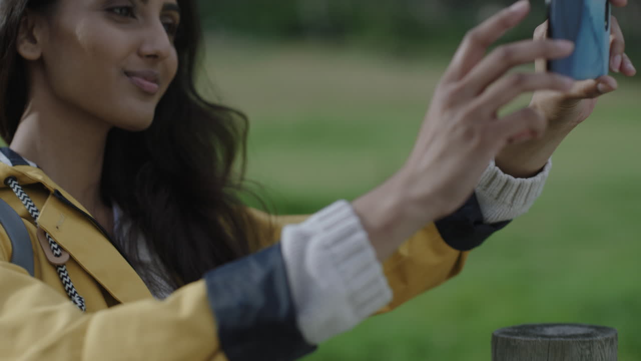 una joven india que toma fotos usando la tecnología de la cámara de su teléfono inteligente disfrutando de compartir aventuras, viajes, caminatas, fotografiando el campo verde al aire libre