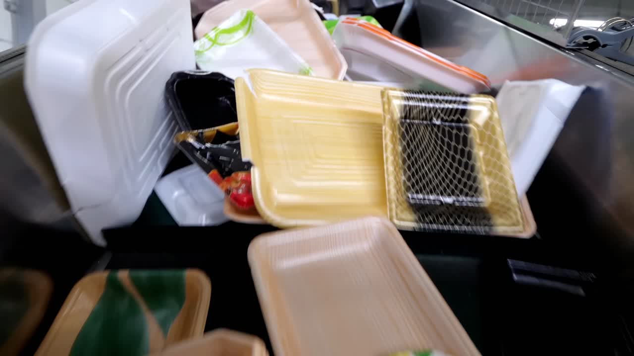 Plastic waste is being recycled at the recycling plant. Plastic boxes, foam, and paper packaging are moving along the conveyor belt of the sorting line.