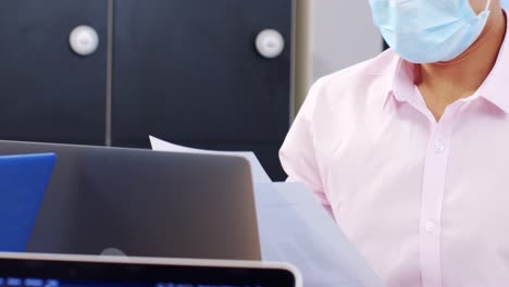 Young-Man-In-Face-Mask-Looking-at-Papers-In-Modern-Office