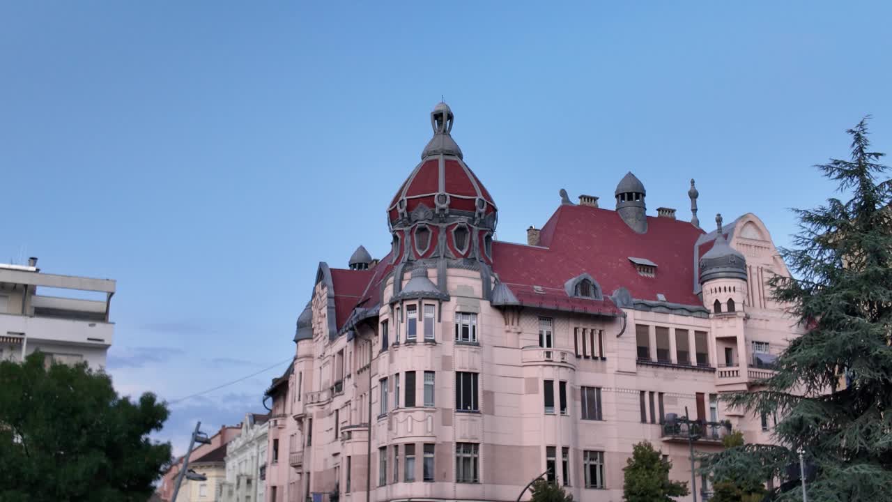 Scenic evening shot of Szeged’s landmark with red rooftop, framed by a fountain spraying water and warm dusk lighting