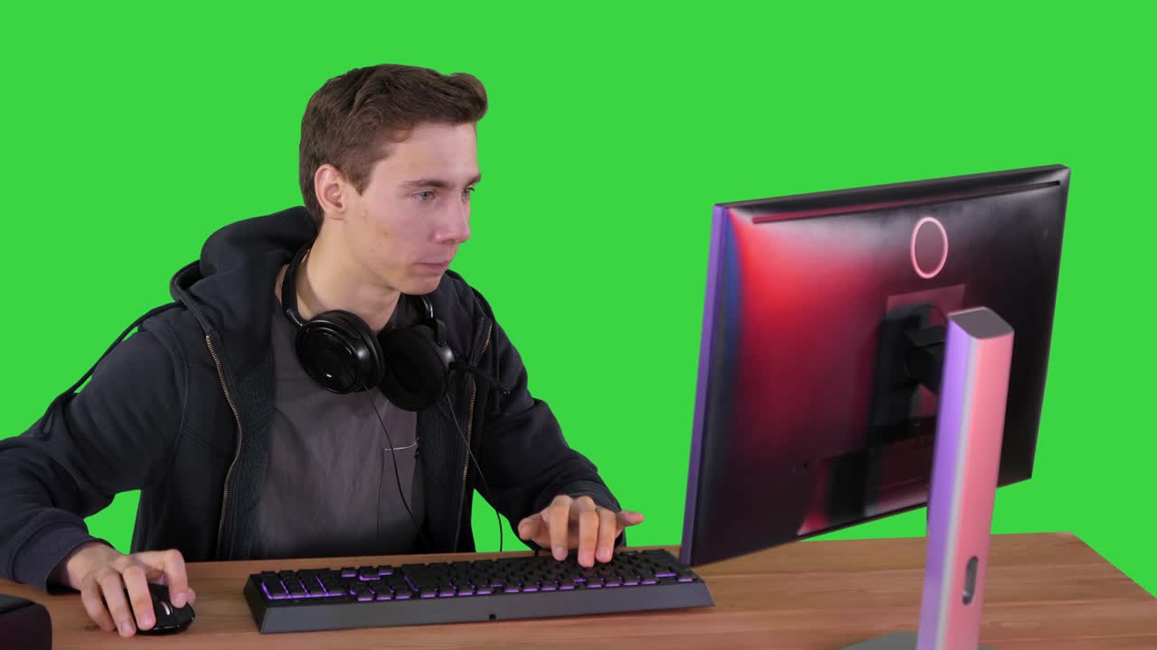 헤드폰을 들고 컴퓨터에서 비디오 게임을 하고 녹색 화면에서 카메라에 엄지손가락을 보여주고 있는 게이머
