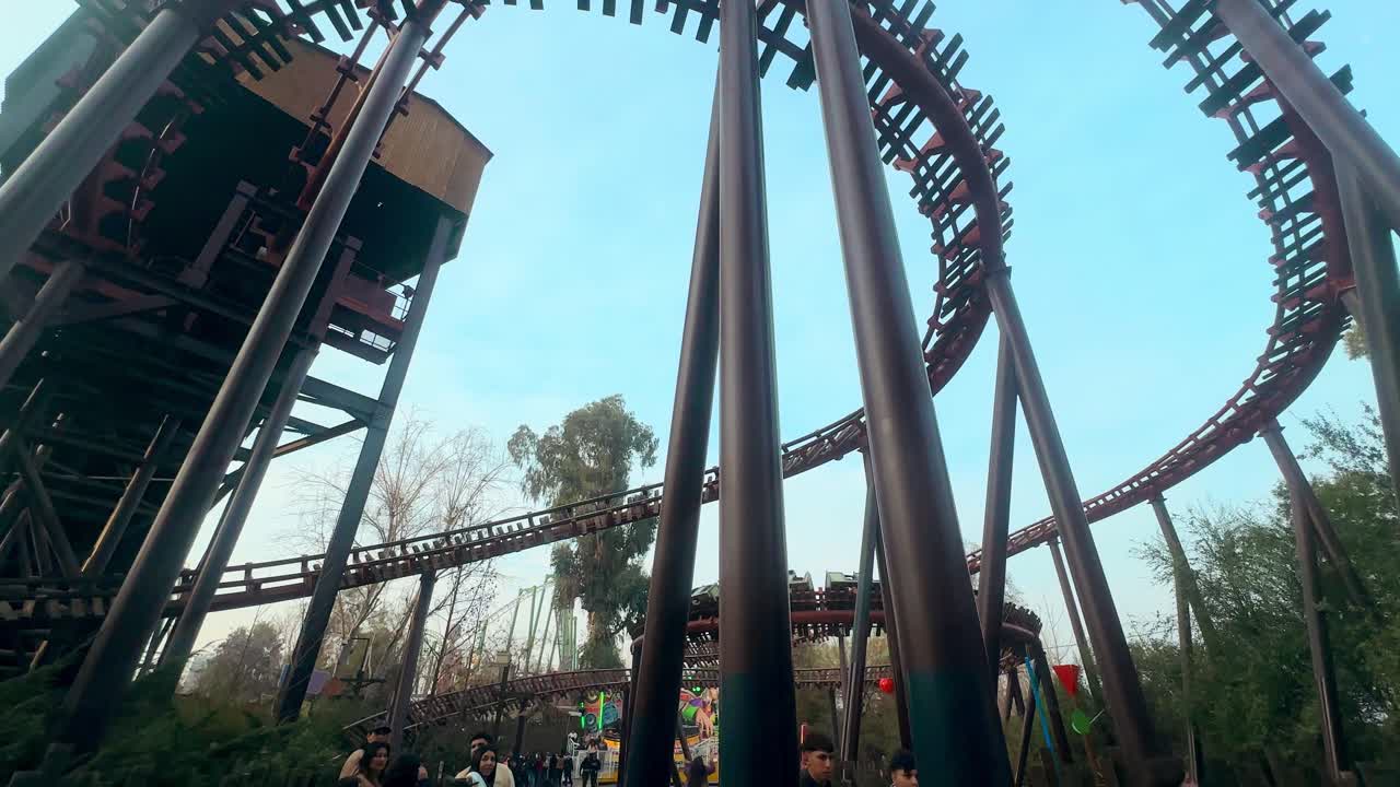 View nadir tracking to a mining train of an amusement park, wooden rails with a group of people walking underneath, Fantasilandia park, Santiago, Chile.
