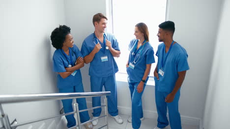 portrait of smiling multi cultural medical team wearing scrubs standing on stairs in hospital